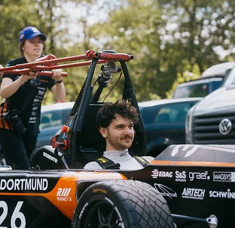 Fahrer lacht im Cockpit, Teammitglied steht daneben